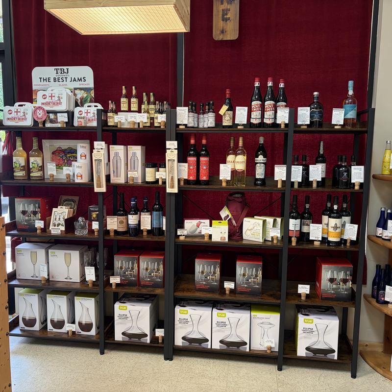 A display wall of specialty bottles, jams, glassware and gift items against a deep red backdrop
